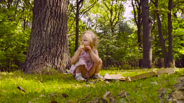 Petite fille assise dans le parc et mangeant de la pizza 