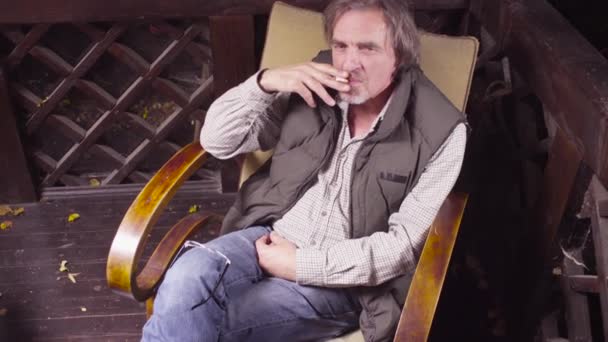Starší muž, sedící v křesle, pije víno a kouření — Stock video