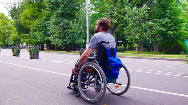 Joven hombre incapacitado caminando en el parque en silla de ruedas —  Fotos de Stock