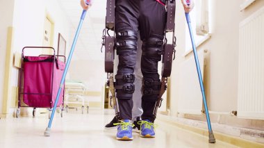 Legs of invalid in robotic exoskeleton walking through the corridor clipart