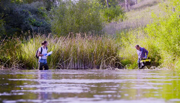 Twee wetenschappers ecologen in hoge rubberen laarzen lopen in het water van de rivier de bos — Stockfoto