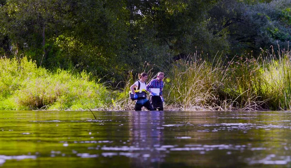 Dos científicos ecologistas en botas altas de goma caminando en el agua del río bosque —  Fotos de Stock
