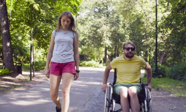Genç adam karısı ile parkta yürüyüş tekerlekli sandalyede devre dışı