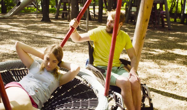 Woman is lying on a swing and a man is pushing a swing — Stock Photo, Image