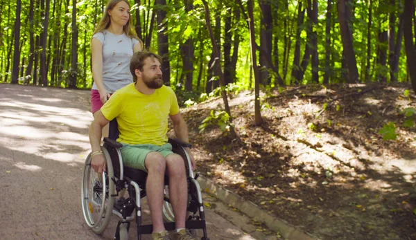 Νέοι απενεργοποιήσετε άνθρωπος σε μια αναπηρική καρέκλα με τα πόδια στο πάρκο με τη σύζυγό του — Φωτογραφία Αρχείου