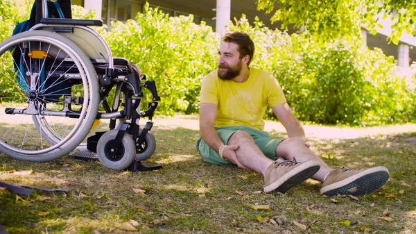 Glücklicher junger behinderter Mann sitzt auf dem Gras im Park — Stockfoto