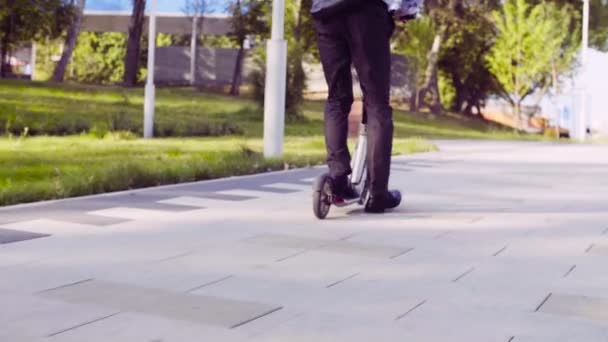 Piernas de un hombre en un traje de negocios montando un patinete scooter — Vídeos de Stock