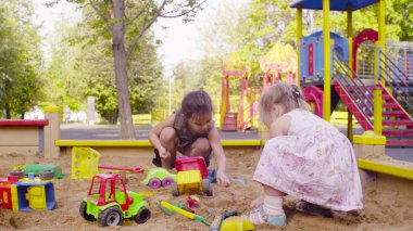 Kum havuzunda oturuyor ve kumu seçmek iki kız