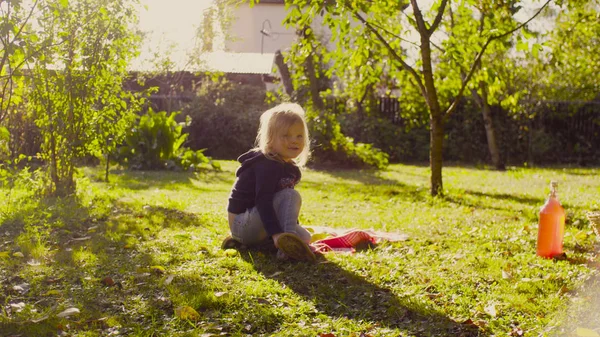 Niña sentada en una hierba en un jardín y poniéndose los zapatos —  Fotos de Stock