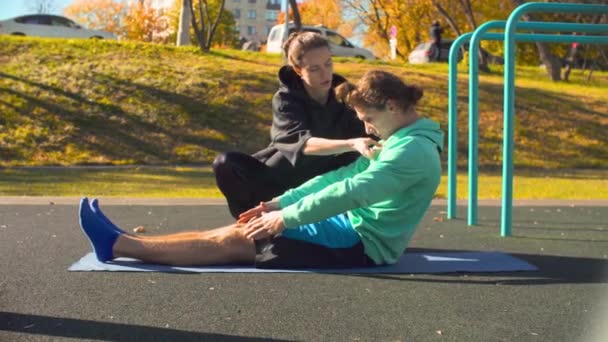 Jeune homme flexible faisant des exercices pour la colonne vertébrale sur le terrain de sport . — Video