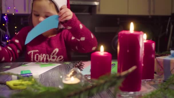 Маленька дівчинка приклеює новорічну листівку — стокове відео