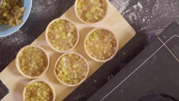 Manos de un pastelero poniendo llama de manzana en tartaletas — Vídeos de Stock