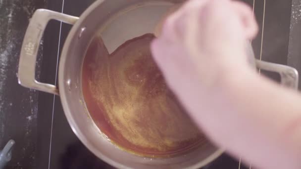 Hände eines Konditors, der Zucker in der Pfanne schmelzen lässt und dann Milch hinzufügt — Stockvideo