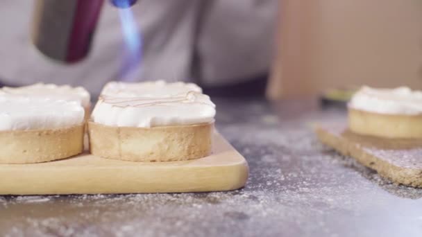 Hands of a confectioner burning swiss meringue on tartlets — Stock Video