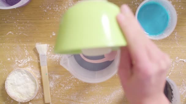 Manos de confitero mezclando diferentes colores de esmalte espejo en un tazón grande — Vídeo de stock