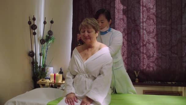 Unga kinesiska läkare gör massage till en äldre kvinna — Stockvideo