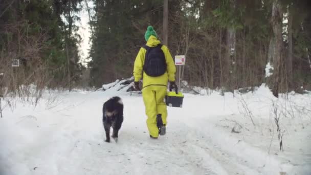 Ecologista con el perro paseando por la carretera en el bosque de invierno — Vídeos de Stock