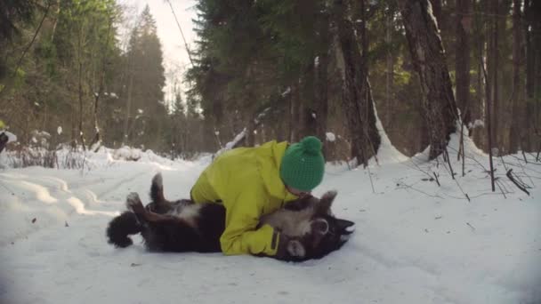 Donna che gioca con il cane sulla neve nella foresta invernale — Video Stock