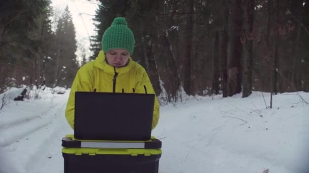 Эколог в спортивной одежде работает на ноутбуке в зимнем лесу — стоковое видео