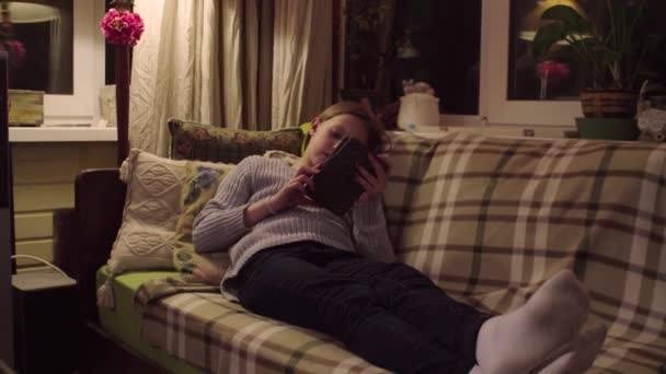 クレーン ショット 少女はソファーに横になっているとの電子書籍を読む — ストック動画
