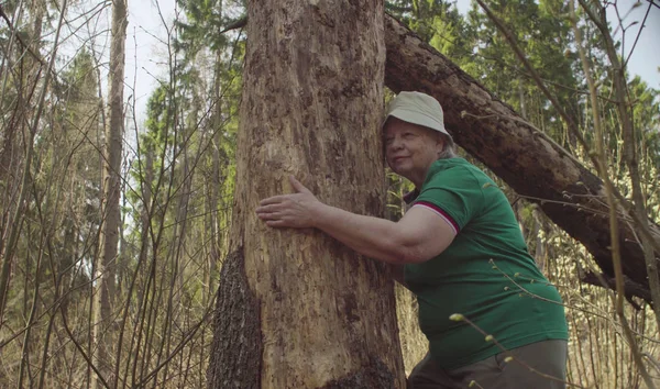 Senior vrouw in het bos knuffelen een beschadigde boom — Stockfoto