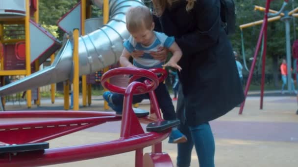 Мать сажает маленького сына на карусель — стоковое видео