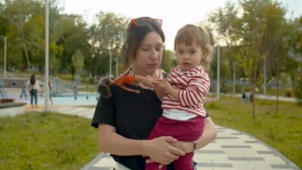ママは彼女の腕の中で小さな女の子と公園を歩く — ストック動画