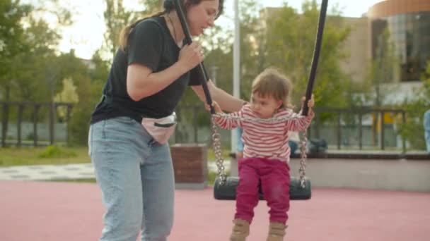 Yakışıklı anne bir salıncak üzerinde küçük kızı iterek — Stok video