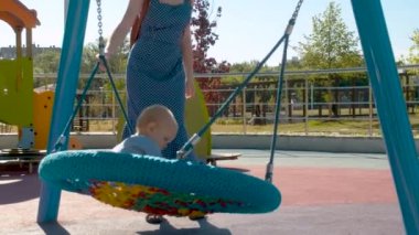 Genç anne küçük çocuğu salıncakta itiyor.
