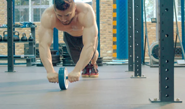 Culturista haciendo ejercicio en gimnasio con rueda abdominales — Foto de Stock