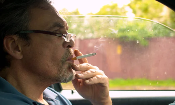 Portrét staršího muže, který řídil auto a kouří — Stock fotografie