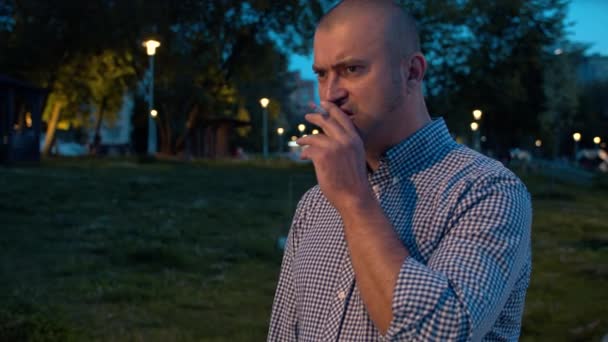 Портрет агрессивного жестокого человека, курящего в парке — стоковое видео