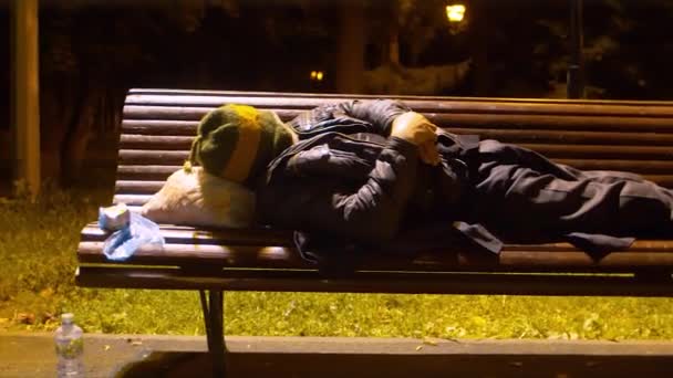 Hombre sin hogar durmiendo en un banco del parque — Vídeo de stock