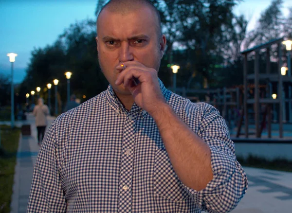 Portrét agresivního brutálního muže, který v parku kouří — Stock fotografie