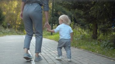 Annesiyle parkta yürüyen bir çocuk.