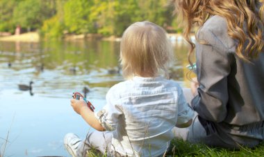 Genç bir anne ve yavrusu göldeki ördekleri besliyor.