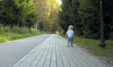 Küçük çocuk parkta yol boyunca yürüyor.