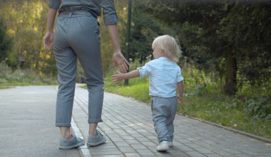 Annesiyle parkta yürüyen bir çocuk.