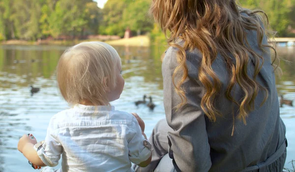 Uma jovem mãe e sua criança estão alimentando os patos em um lago — Fotografia de Stock