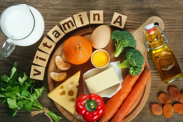 Vitamin A in food. Natural products rich in vitamin A as tangerine, red pepper, parsley leaves, dried apricots, carrots, broccoli, butter, yellow cheese, milk, egg yolk and cod liver oil. Wooden table as background.