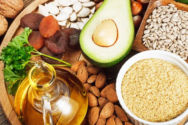 Foods rich in vitamin E such as wheat germ oil, dried wheat germ, dried apricots, hazelnuts, almonds, parsley leaves, avocado, walnuts, pumpkin seeds, sunflower seeds on wooden table