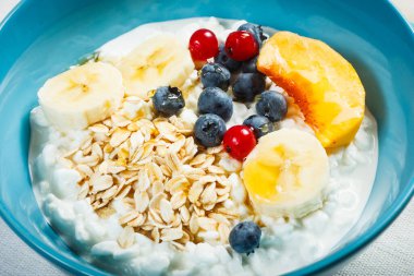 Sağlıklı kahvaltı. Granüle edilmiş süzme peynir artı yulaf gevreği, muz, yabanmersini, frenk üzümü, şeftali ve bal..
