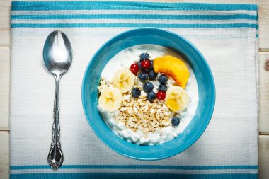 Sağlıklı kahvaltı. Granüle edilmiş süzme peynir artı yulaf gevreği, muz, yaban mersini, frenk üzümü, şeftali ve bal. Fotoğraf klasik tarzda.
