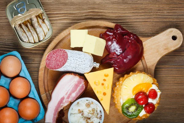 Yumurta, ciğer, sarı peynir, tereyağı, pastırma, soğanlı domuz yağı, yağlı sardalya ve kremalı kek gibi yüksek kolesterollü gıdalar. Arkaplan olarak tahta tablo