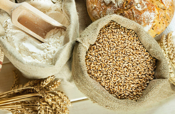Loaf of bread, flour, wheat grain and wheat spike on table