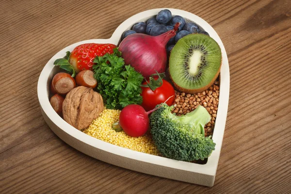 Healthy food in heart shaped bowl. Food such as blueberries, red onion, strawberry, parsley leaves, hazelnuts, walnut, tomato. kiwi, millet, buckwheat, radish, broccoli