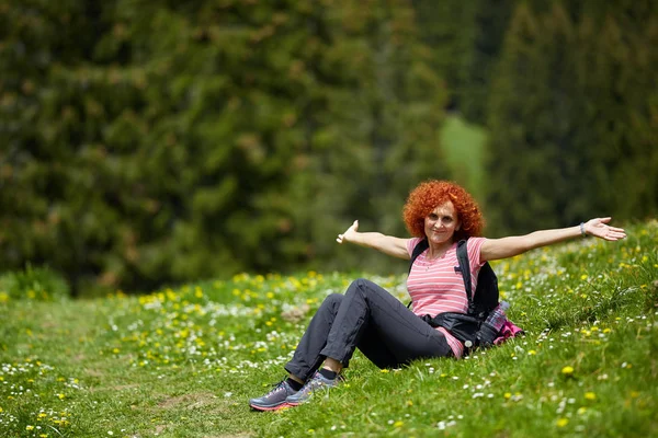 女性ハイカーのバックパックを草 長いハイキングの後に休憩で座っています — ストック写真