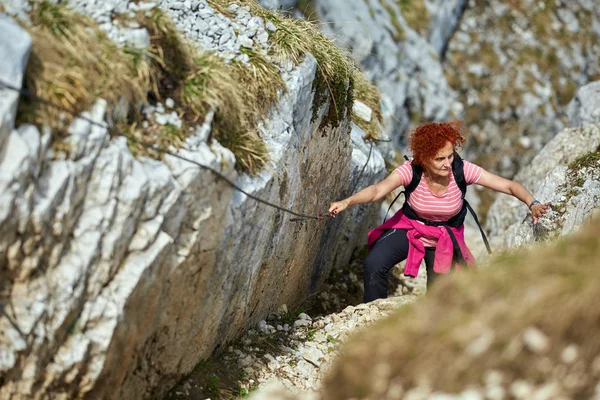 Woman holding rope and free climbing on via ferrata in rocky mountains