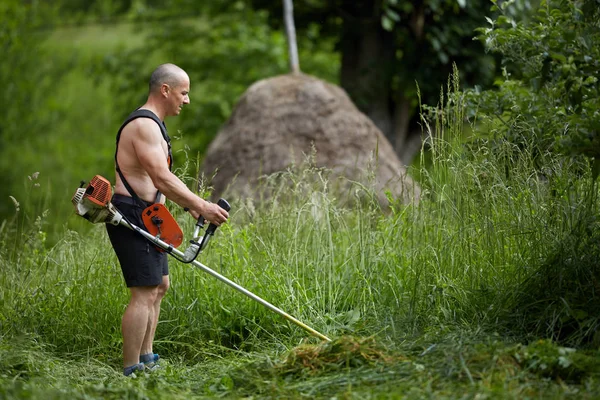 草刈機 電動の芝刈り機で土地を刈る男 — ストック写真