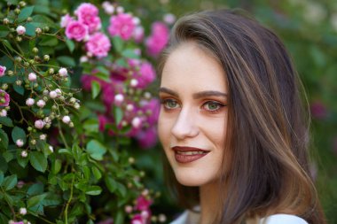 Bahçesinde gül bush yakınındaki beyaz elbiseli genç gülümseyen kadın closeup